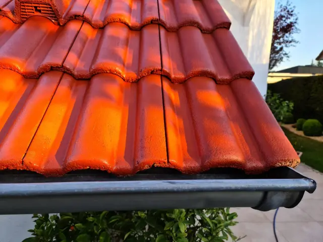 Nahaufnahme eines frisch beschichteten, rot-orangen Ziegeldachs; saubere Kanten bis zur Dachrinne.