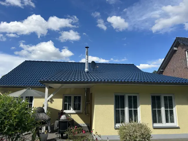 Gelbes Einfamilienhaus mit blau beschichtetem Ziegeldach; sichtbare Detailarbeiten an Kamin, Sat-Schüssel und Dachanschlüssen.